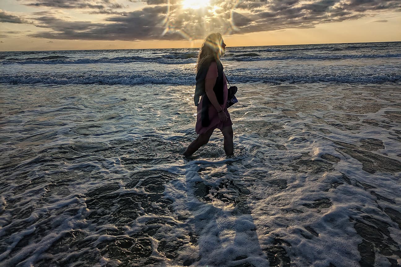 Rhianna walking through ocean surf at sunset, with sunburst halo